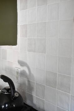 a black tea kettle sitting on top of a stove next to a white tiled wall