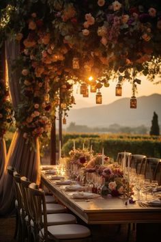 an outdoor dining table set up with candles and flowers on the tables, along with hanging lanterns