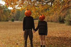 two people holding hands with pumpkins on their heads in front of a tree filled with leaves