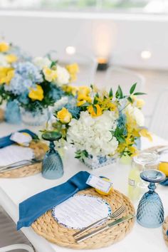 the table is set with yellow and white flowers, blue napkins, and silverware