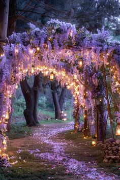 an archway decorated with purple flowers and lit candles in the middle of it is surrounded by trees