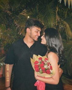 a man holding a bouquet of red roses next to a woman with long dark hair