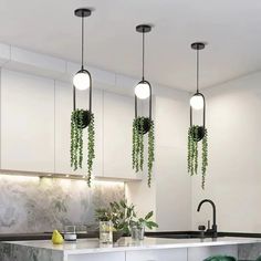 three lights hanging from the ceiling above a kitchen island with stools and plants on it