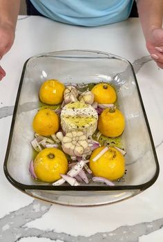 a glass dish with lemons, cauliflower and onions in it on a marble countertop