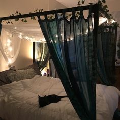 an unmade bed with green curtains and lights on the headboard, in a bedroom