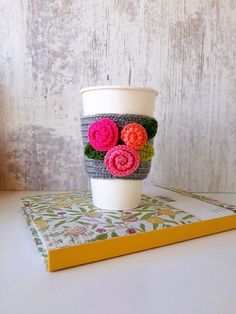 a coffee cup with crocheted flowers on it sitting on top of a book