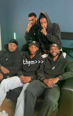 four men are sitting on a couch posing for the camera with their hoodies up