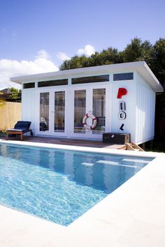 a small pool house with a deck and lounge chairs next to it