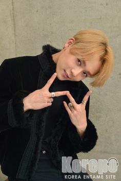 a young man making the v sign with his fingers while wearing a black jacket and fur coat