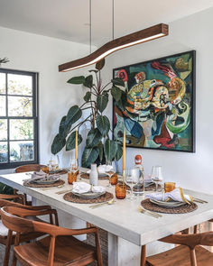 a dining room table with plates and place settings on it in front of a painting