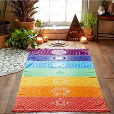 a rainbow rug on the floor in front of a window with candles and potted plants