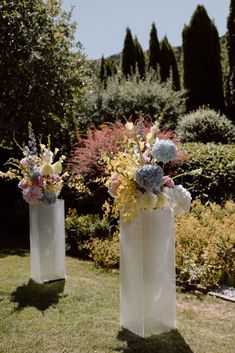 two white vases with flowers in them on the grass