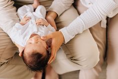 a woman is holding a baby in her lap and touching it's head with both hands