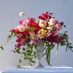 a vase filled with lots of pink and red flowers on top of a blue table cloth