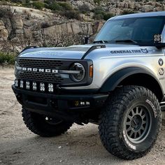 a silver and black truck parked on top of a dirt field next to some rocks