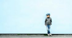 a young boy standing in front of a blue wall with his hands on his hips