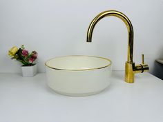 a sink with a gold faucet next to a white bowl and some flowers