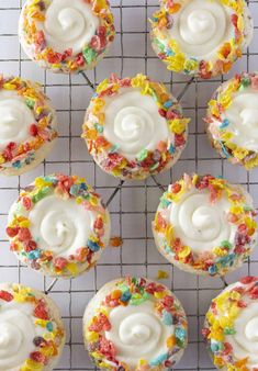 several cupcakes with white frosting and sprinkles on a cooling rack