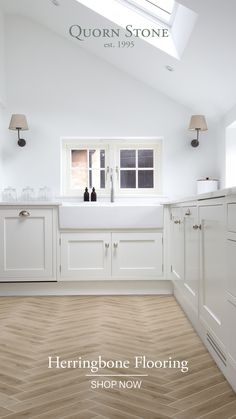 an empty kitchen with white cabinets and wood flooring is pictured in this image, there are two wine bottles on the window sill