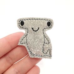 a hand holding a silver glittered brooch with a cute little creature on it's back