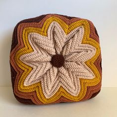 a crocheted square with a flower on the center is shown in brown, yellow and white