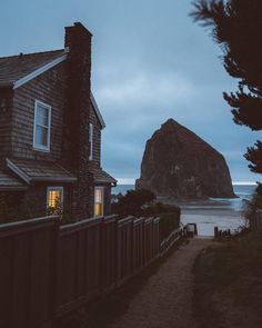 a house next to the ocean with a large rock in the background