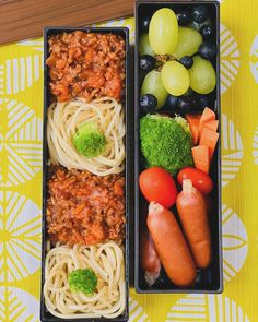 two black trays filled with food on top of a yellow and white table cloth