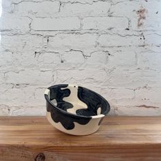 a black and white bowl sitting on top of a wooden table next to a brick wall