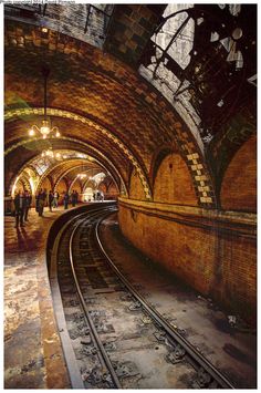 an old train station with people walking on the platform and tracks in front of it