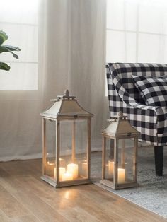 two lit candles sitting on top of a wooden floor next to a chair and window