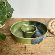 two green bowls sitting on top of a wooden table next to a potted plant