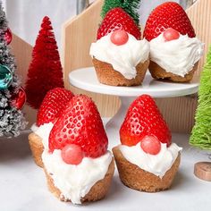 three cupcakes with white frosting and strawberries on top, next to a christmas tree