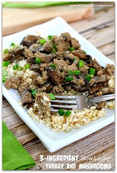 a white plate topped with rice covered in meat and green onions next to a fork