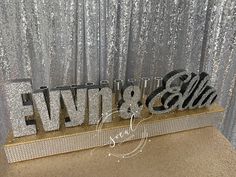 the letters are made out of silver glitters and sit in front of a curtain