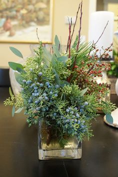 a vase filled with lots of green and red flowers on top of a black table