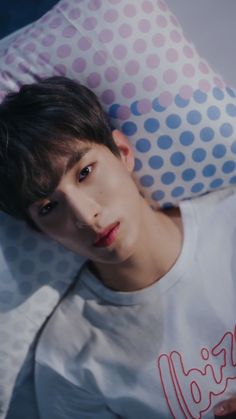 a young man laying on top of a bed under a polka dot pillow with his eyes closed