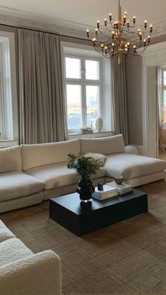 a living room filled with furniture and a chandelier hanging from the ceiling in front of two large windows