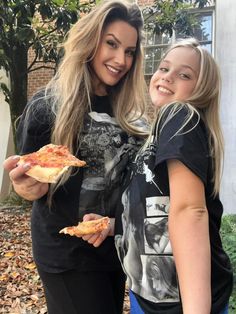 two girls are posing for the camera while eating pizza