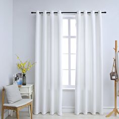 a white curtain hanging on the side of a window next to a chair and table