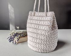 a white crocheted bag next to a book and some lavenders on a table