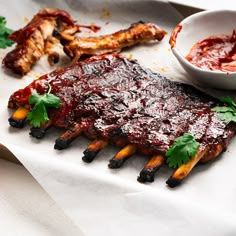 ribs with sauce and garnishes on a white paper towel next to a bowl of ketchup