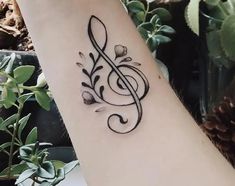 a black and white photo of a musical note tattoo on the arm, with flowers around it