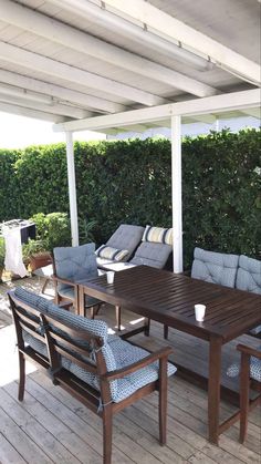 a wooden table sitting on top of a wooden deck next to a white wall covered in greenery