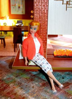 a doll sitting on top of a table in front of a red and white cake