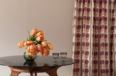 a vase with orange flowers sitting on top of a table next to two wine glasses