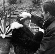 a man and woman sitting on a bench next to each other with plants in the background