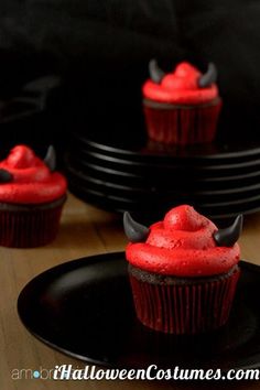 cupcakes with red frosting and horns on them are sitting on black plates