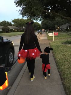 a woman walking down a sidewalk with a child wearing minnie mouse costumes on her feet