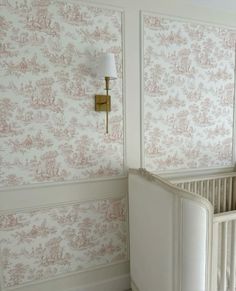 a baby crib next to a wall with pink and white wallpaper on it