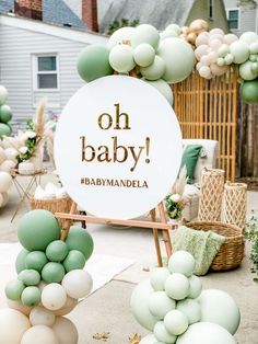 an outdoor baby shower with green and white balloons, greenery and a sign that says oh baby